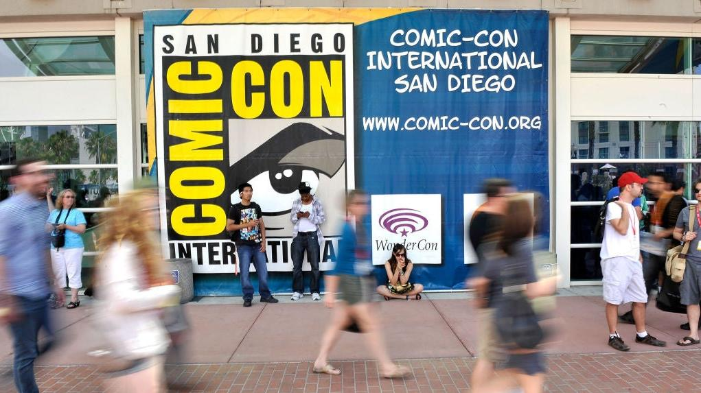 Ett foto av en SDCC-banner utanför San Diego Convention Center med olika fans som går och suddas i förgrunden.